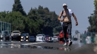 Seorang pejalan kaki terlihat membuka kaos untuk mendinginkan badan selama cuaca panas ekstrem di Yuba City, California, Amerika Serikat, Jumat (30/6/2023).