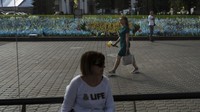 Seorang wanita dengan bunga berjalan melewati situs peringatan untuk menghormati orang yang terbunuh dalam serangan Rusia di Kyiv, Ukraina, Senin, 3 Juli 2023.  