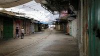 Warga Palestina berjalan melewati toko-toko yang tutup.