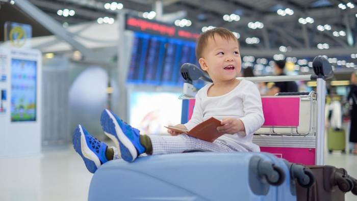 Little traveler, Cute Asian 18 months / 1 year old toddler boy child holding passport with suitcase, sitting on trolley at airport, waiting for departure, Family travel & vacation with kid concept