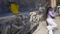 Seorang wanita berdiri di dekat air mancur kering dengan plakat bertuliskan dialek Romawi: Tidak ada yang peduli padaku, menggunakan kipas angin untuk menghindari panasnya sore yang cerah di dekat Colosseum Roma, Italia, Rabu (5/7/2023).