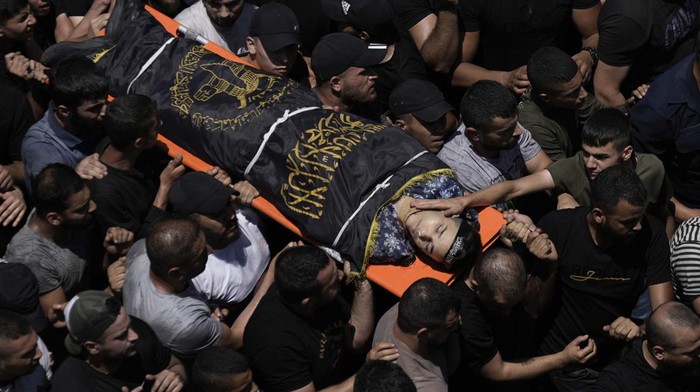 Ribuan Orang Anter Pemakaman Korban Tewas Serangan Israel Mourners carry the body of a Palestinian man draped in the flag of the Islamic Jihad militant group during their funeral, in the Jenin refugee camp, West Bank, Wednesday, July 5, 2023. The Israeli military says it withdrew its troops from the camp on Wednesday, ending an intense two-day operation that killed at least 13 Palestinians, drove thousands of people from their homes and left a wide swath of damage in its wake. One Israeli soldier was also killed. (AP Photo/Majdi Mohammed)