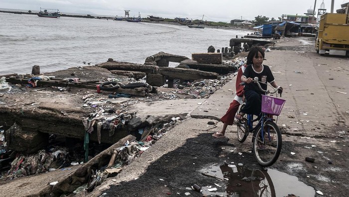 Pengendara motor melintas di samping dermaga yang rusak di Teluk Labuan, Pandeglang, Banten, Kamis (6/7/2023). Fasilitas dermaga tempat berlabuh kapal nelayan tersebut kondisinya rusak berat akibat diterjang gelombang tinggi yang terjadi beberapa hari terakhir. ANTARA FOTO/Muhammad Bagus Khoirunas/Spt.