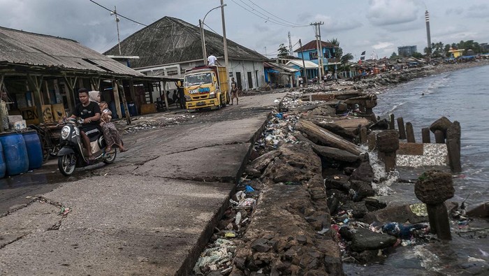 Pengendara motor melintas di samping dermaga yang rusak di Teluk Labuan, Pandeglang, Banten, Kamis (6/7/2023). Fasilitas dermaga tempat berlabuh kapal nelayan tersebut kondisinya rusak berat akibat diterjang gelombang tinggi yang terjadi beberapa hari terakhir. ANTARA FOTO/Muhammad Bagus Khoirunas/Spt.