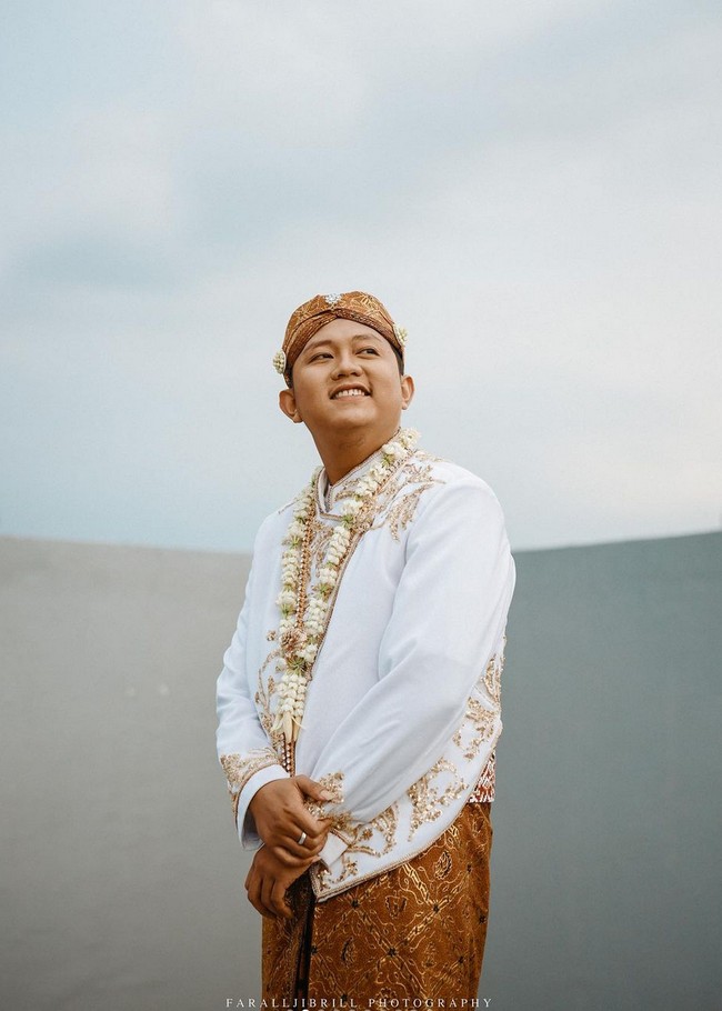Denny Caknan mengenakan beskap putih yang juga dihiasi bordir dan payet. Penyanyi dangdut koplo ini melengkapi penampilannya dengan blangkon batik yang dihiasi bunga melati. Foto: Instagram/@faralljibrill_official
