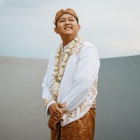 Denny Caknan mengenakan beskap putih yang juga dihiasi bordir dan payet. Penyanyi dangdut koplo ini melengkapi penampilannya dengan blangkon batik yang dihiasi bunga melati. Foto: Instagram/@faralljibrill_official