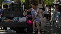 Seorang wanita menggunakan kipas angin untuk menyejukkan seorang anak saat mereka duduk di bangku di jalan perbelanjaan pejalan kaki Qianmen. AP/Andy Wong  