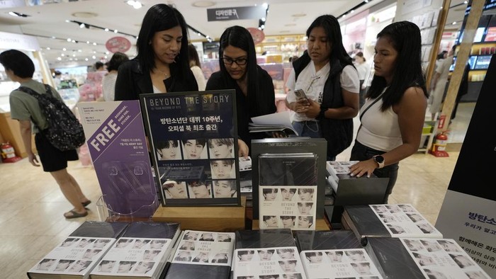 BTS Luncurkan Buku Memoar 10 Tahun Berkarya Women look at copies of