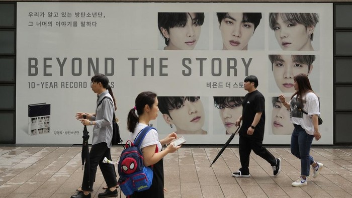 BTS Luncurkan Buku Memoar 10 Tahun Berkarya Women look at copies of