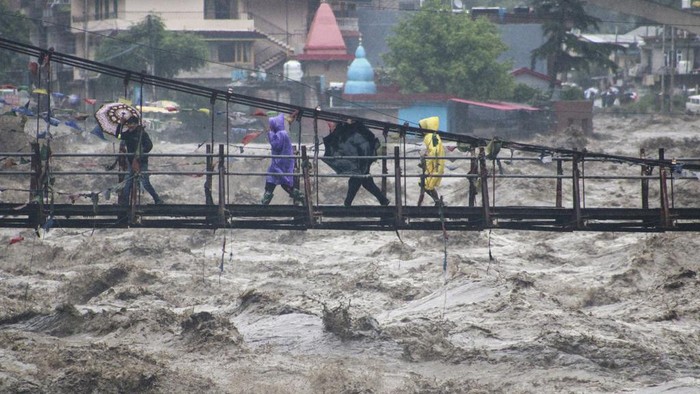 Badai di India Sebabkan Banjir Bandang hingga Longsor People walk across a bridge over the River Beas swollen due to heavy rains in Kullu District, Himachal Pradesh, India, Monday, July 10, 2023. Indiaβs weather agency has forecast more heavy rains in the north in the coming days. (AP Photo/ Aqil Khan)