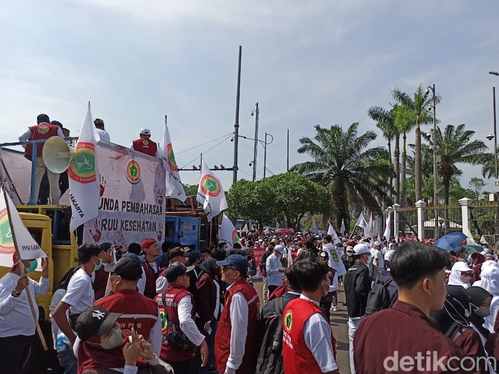 [Sejumlah massa dari organisasi profesi mendatangi Gedung DPR untuk menolak RUU Kesehatan. Para pedemo mengenakan kaos dan kemeja berwarna putih yang bertuliskan 'Stop RUU Kesehatan'.]