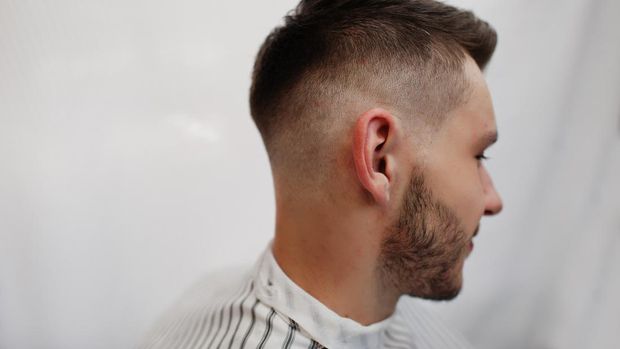fade undercut Close up head of young bearded man getting haircut at barbershop. Barber soul.