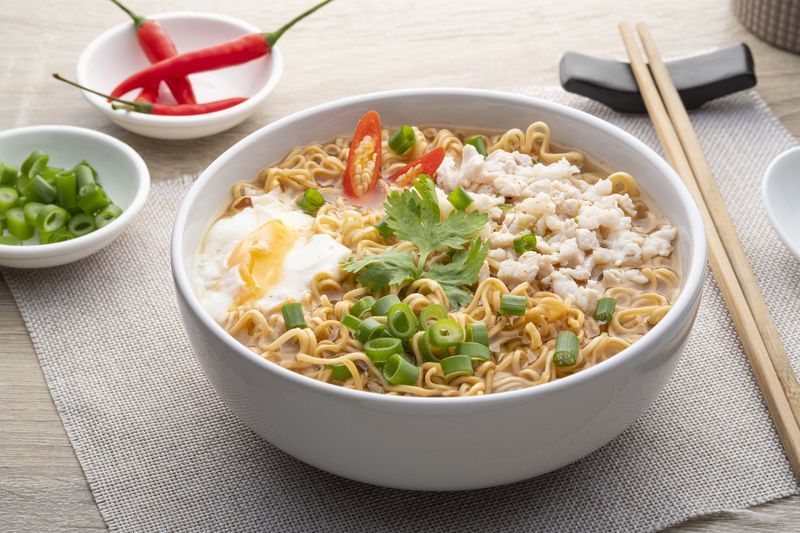 Instant noodle soup with minced pork and boiled egg in white bowl on wood table