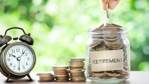Hand putting Coins in glass jar with retro alarm clock  for time to money saving for retirement concept