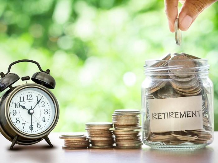 Hand putting Coins in glass jar with retro alarm clock  for time to money saving for retirement concept
