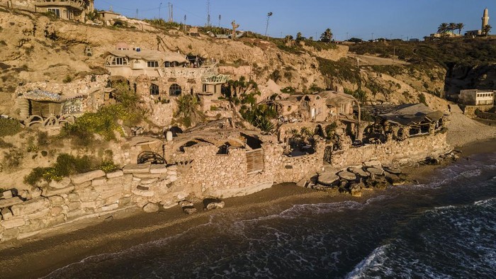 Pria Ini Bangun Rumah Gua di Tebing Batu Israel, Begini Bagian Dalamnya Nissim Kahlon sits in his balcony in his home chiseled out of the sandstone cliffs overlooking the Mediterranean sea in Herzliya, Israel, Wednesday, June 28, 2023. Over half a century, Kahlon has transformed a tiny cave on a Mediterranean beach into an elaborate underground labyrinth filled with chiseled tunnels, detailed mosaic floors and a network of staircases and mysterious chambers. Fifty years after Kahlon moved into the home, Israel's Environmental Protection Agency has served him an eviction notice, claiming the structure threatens Israel's coastline. (AP Photo/Ariel Schalit)