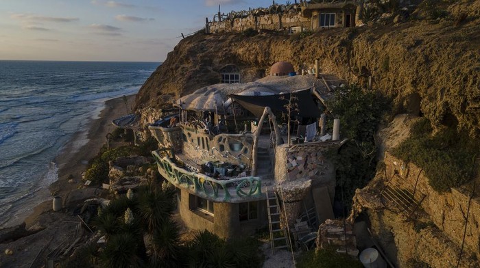 Nissim Kahlon sits in his balcony in his home chiseled out of the sandstone cliffs overlooking the Mediterranean sea in Herzliya, Israel, Wednesday, June 28, 2023. Over half a century, Kahlon has transformed a tiny cave on a Mediterranean beach into an elaborate underground labyrinth filled with chiseled tunnels, detailed mosaic floors and a network of staircases and mysterious chambers. Fifty years after Kahlon moved into the home, Israel's Environmental Protection Agency has served him an eviction notice, claiming the structure threatens Israel's coastline. (AP Photo/Ariel Schalit)
