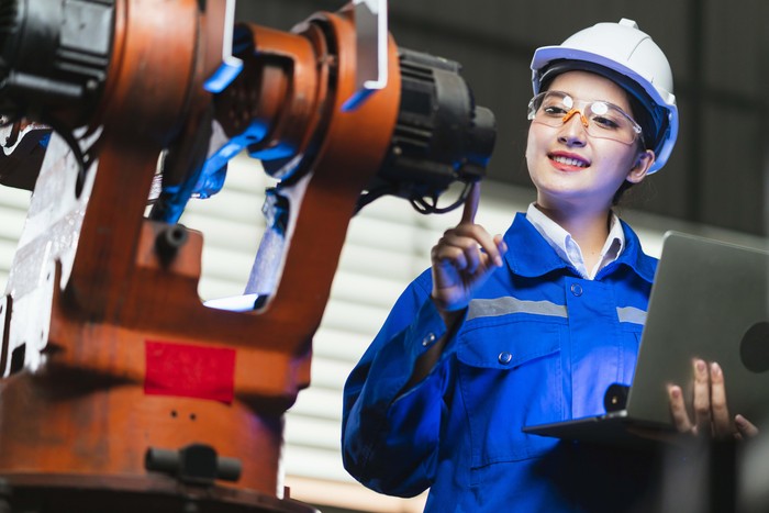 engineer specialist asian female and technician maintenance inspect relay robot arm system with laptop to control quality operate process work heavy industry 4.0 manufacturing smart factory