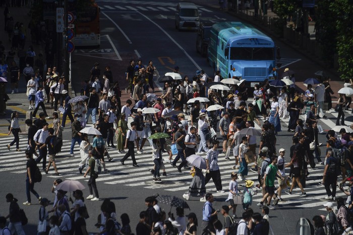 People carry umbrellas to shield themselves from the intense heat from the sun as they walk across an intersection Wednesday, July 12, 2023, in Tokyo. (AP Photo/Kiichiro Sato)