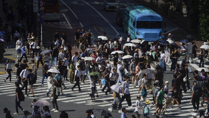 People carry umbrellas to shield themselves from the intense heat from the sun as they walk across an intersection Wednesday, July 12, 2023, in Tokyo. (AP Photo/Kiichiro Sato)