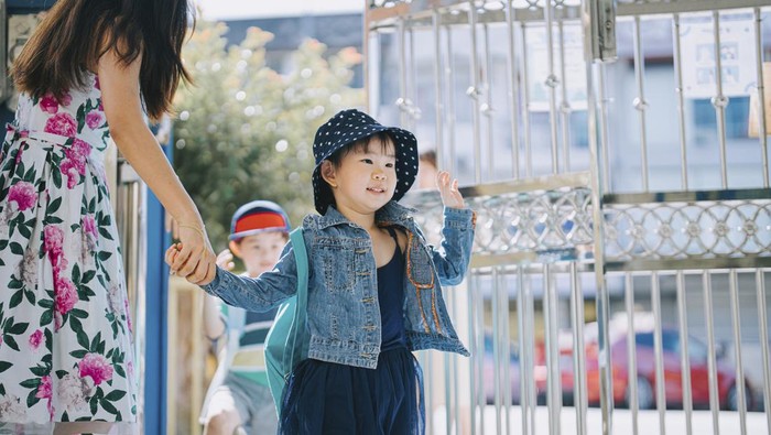 Asian chinese preschool teacher welcoming their student entering through front gate in the morning