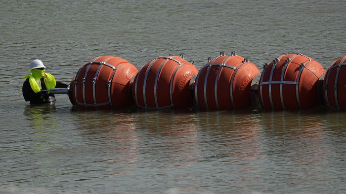 Texas Pasang Penghalang Apung di Sungai untuk Cegah Migran Menyebrang Workers continue to deploy large buoys to be used as a border barrier along the banks of the Rio Grande in Eagle Pass, Texas, Wednesday, July 12, 2023. The floating barrier is being deployed in an effort to block migrants from entering Texas from Mexico. (AP Photo/Eric Gay)