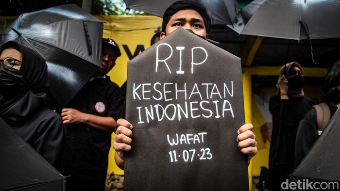 Massa menggelar aksi damai menolak UU Kesehatan yang baru disahkan. Sambil membawa payung, massa aksi di seberang kantor Kemenkes, Jakarta.