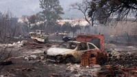 Mobil-mobil hangus terbakar imbas kebakaran hutan. Awan asap terlihat di atas desa-desa dari pantai wisata terdekat.