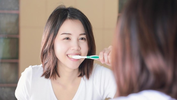 Young woman brushing her teeth at mirror. After awakening