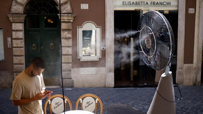 A man called David checks his phone as he stands near a fan to cool off, during a heatwave across Italy, in Rome, July 14, 2023. REUTERS/Guglielmo Mangiapane