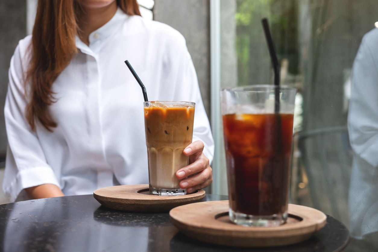 Closeup image of a woman holding a cup of iced coffee on the table in cafe