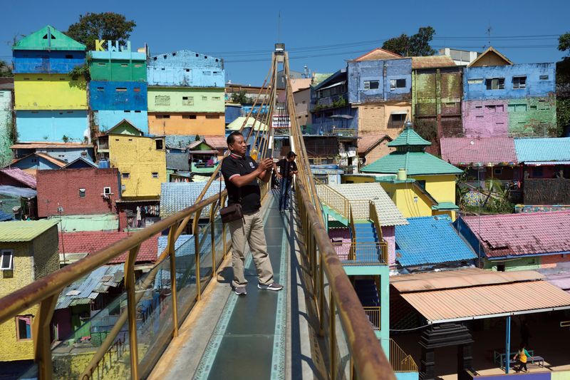 Wisatawan berjalan di jembatan kaca saat mengunjungi Kampung Warna-Warni Jodipan di Malang, Jawa Timur, Kamis (20/7/2023). Kampung warna-warni yang dibuka sebagai objek wisata sejak tahun 2016 tersebut saat ini dicat ulang secara bertahap pada ratusan rumah milik warga setempat yang dimulai dari awal tahun 2023 untuk meningkatkan jumlah kunjungan wisata. ANTARA FOTO/Nyoman Hendra Wibowo/rwa.