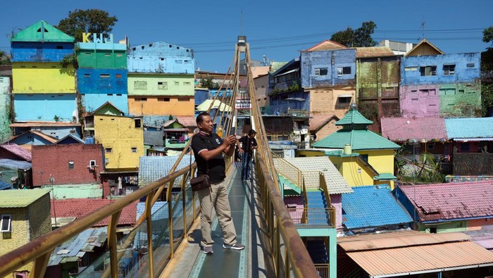 Wisatawan berjalan di jembatan kaca saat mengunjungi Kampung Warna-Warni Jodipan di Malang, Jawa Timur, Kamis (20/7/2023). Kampung warna-warni yang dibuka sebagai objek wisata sejak tahun 2016 tersebut saat ini dicat ulang secara bertahap pada ratusan rumah milik warga setempat yang dimulai dari awal tahun 2023 untuk meningkatkan jumlah kunjungan wisata. ANTARA FOTO/Nyoman Hendra Wibowo/rwa.