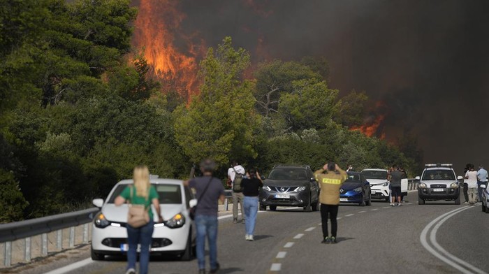 Yunani Kerahkan Pesawat dan Helikopter Pemadam Jinakkan Kebakaran Hutan A fire burns trees next of a road with people and vehicles at the village of Agia Sotira near Athens, on Tuesday, July 18, 2023. In Greece, where a second heatwave is expected to hit Thursday, three large wildfires burned outside Athens for a second day. Thousands of people evacuated from coastal areas south of the capital returned to their homes Tuesday when a fire finally receded after they spent the night on beaches, hotels and public facilities. (AP Photo/Thanassis Stavrakis)