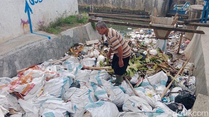 Petugas pintu air sungai Ciloseh tengah memunguti sampah di sungai.