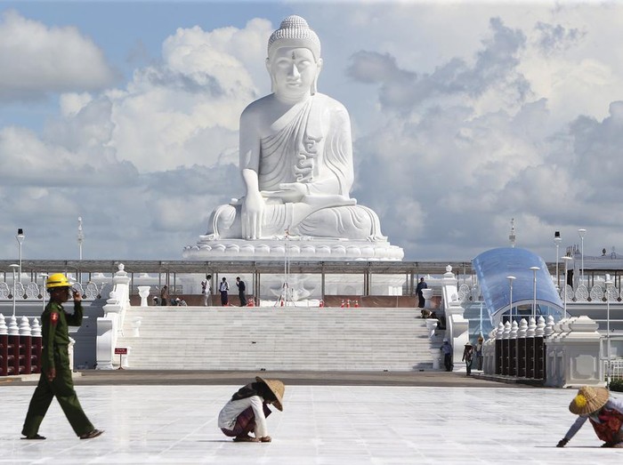 Laborers work while visitors stand below the sitting Maravijaya Buddha marble statue, Friday, July 21, 2023, in Naypyitaw, Myanmar. The Maravijaya Buddha statue is said to be the world’s highest sitting marble Buddha image according to local media. (AP Photo/Aung Shine Oo)