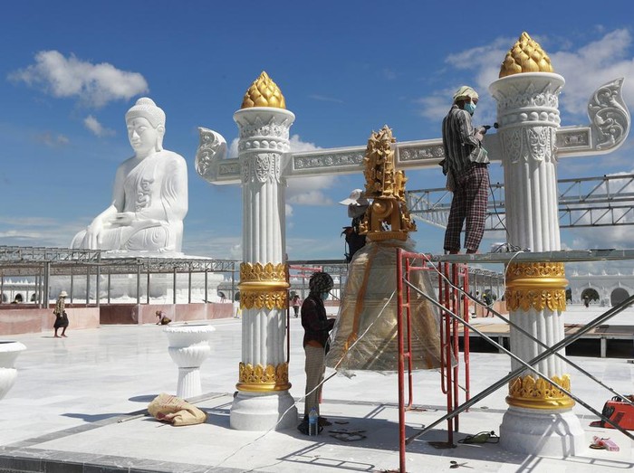 Laborers work while visitors stand below the sitting Maravijaya Buddha marble statue, Friday, July 21, 2023, in Naypyitaw, Myanmar. The Maravijaya Buddha statue is said to be the world’s highest sitting marble Buddha image according to local media. (AP Photo/Aung Shine Oo)