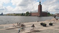 Orang-orang beristirahat di bangku di bawah sinar matahari di pulau Riddarholmen dengan latar belakang Balai Kota di Stockholm. Ada tiga situs warisan dunia yang diakui UNESCO di Stockholm antara lain, Istana Drottningholm, situs Zaman Viking di Birka dan Hovgården, serta pemakaman hutan Skogskyrkogården. REUTERS/Tom Little