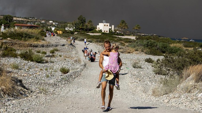 A man carries a child as they leave an area where a forest fire burns, on the island of Rhodes, Greece, Saturday, July 22, 2023. A large wildfire burning on the Greek island of Rhodes for a fifth day has forced authorities to order an evacuation of four locations, including two seaside resorts. (Lefteris Diamanidis/InTime News via AP)