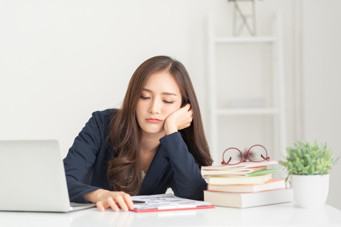 Bored young Asian business woman working with a laptop in the white room. Overworked, tired, Lazy employee at workplace in the office.