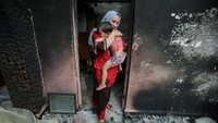 Souhila Belkati menggendong anaknya di dalam rumahnya yang terbakar.  