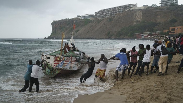Kapal Migran Terbalik di Lepas Pantai Senegal, 17 Orang Tewas People work together to pull, according to the locals, the capsized boat ashore at the beach where several people were found dead in Dakar, Senegal, Monday, July 24, 2023. The bodies were discovered by the navy early in the morning and are believed to be migrants because of the type of boat they were in according to the authorities. (AP Photo/Leo Correa)