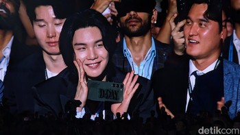 Suga yang hadir secara langsung sempat disorot kamera. Ia terlihat mengacungkan jempolnya dan memperlihatkan ponsel Samsung-nya yang dibalut case bertuliskan D-DAY. Foto: Virgina Maulita Putri/detikinet