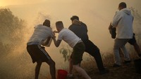 Penduduk setempat menggunakan ember berisi air membantu memadamkan api yang mendekat ke rumah mereka.
