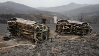 Warga berdiri di dekat mobil yang terbakar akibat kebakaran hutan di Bejaia, Aljazair, 25 Juli 2023.  