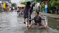 Seorang anak laki-laki mengendarai becak mengarungi jalan yang banjir di Valenzuela, Metro Manila, Filipina, Kamis (27/7/2023). (REUTERS/Eloisa Lopez)