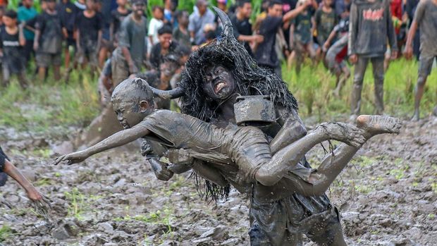 Warga yang berdandan seperti kerbau menceburkan penonton ke dalam lumpur sawah pada tradisi Kebo-keboan Alas Malang di Banyuwangi, Jawa Timur, Minggu (30/7/2023). Tradisi yang dilaksanakan setiap tanggal 10 Suro pada penanggalan Jawa itu digelar sebagai penolak bala sekaligus wujud syukur masyarakat setempat atas rezeki dan panen yang telah diperoleh. ANTARA FOTO/Budi Candra Setya/YU