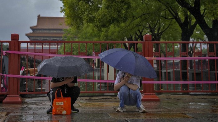 Visitors covered up with umbrellas and rain covers gather at a closed Palace Museum store near the closed Forbidden City as a rainstorm soak Beijing, Sunday, July 30, 2023. Forbidden City and other tourist destinations in the capital city was ordered to close after authorities issued a red alert for rainstorms, as heavy rains brought by Typhoon Doksuri are expected to pound the Chinese capital and vast areas in the north. (AP Photo/Andy Wong)