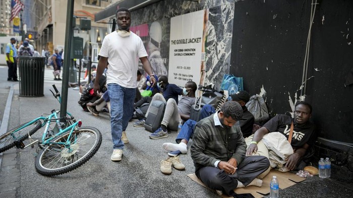 Migrants sit in a queue outside of The Roosevelt Hotel that is being used by the city as temporary housing, Monday, July 31, 2023, in New York. (AP Photo/John Minchillo)