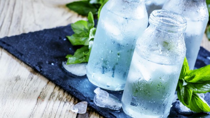 Very cold mineral water with ice in a misted glass bottles, dark background, selective focus